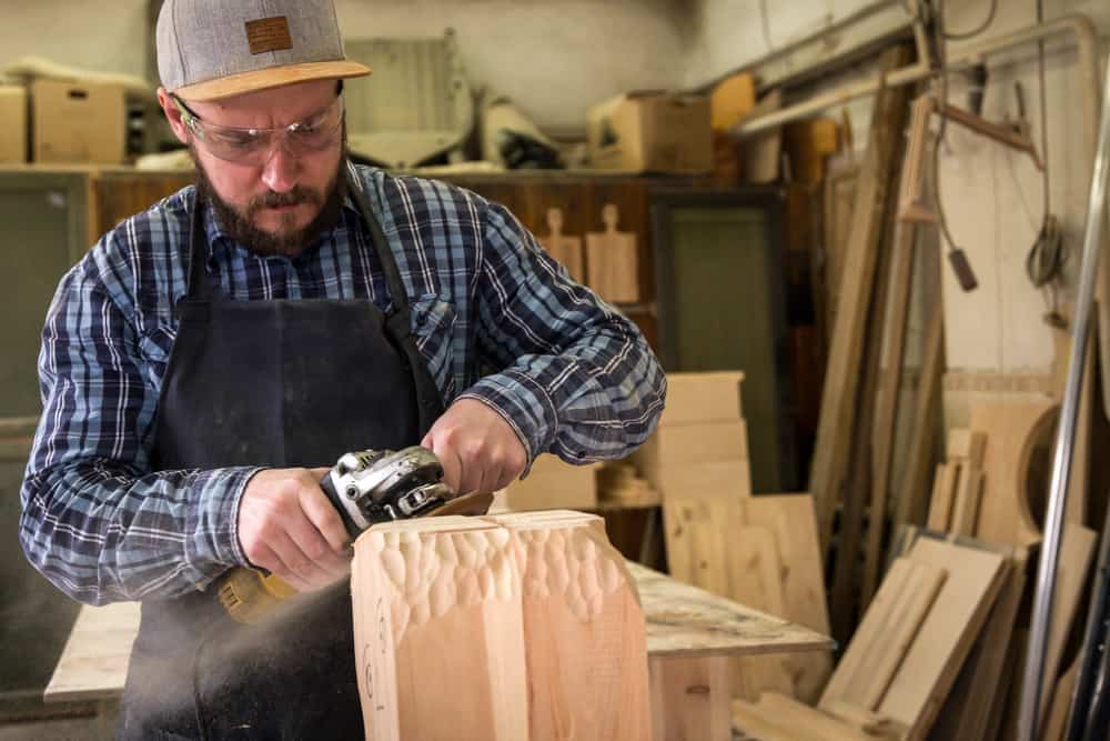 man carving wooden block with an angle grinder