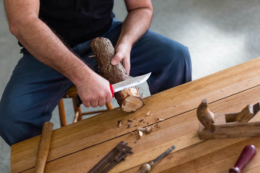 man carving wood with knife