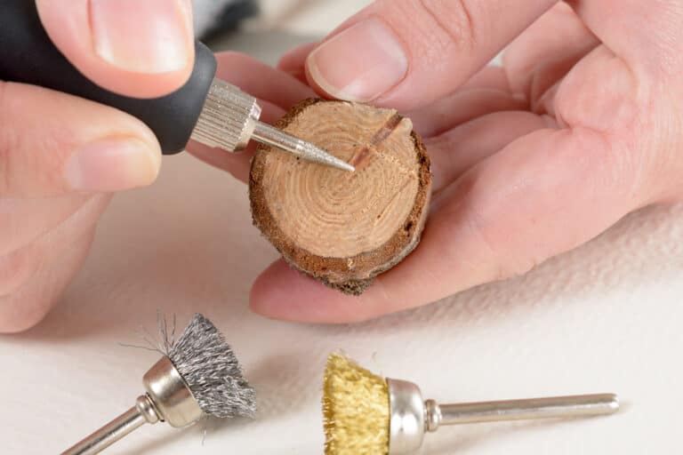 Woman using a high speed rotary multi tool to engrave ornament on slice of wood