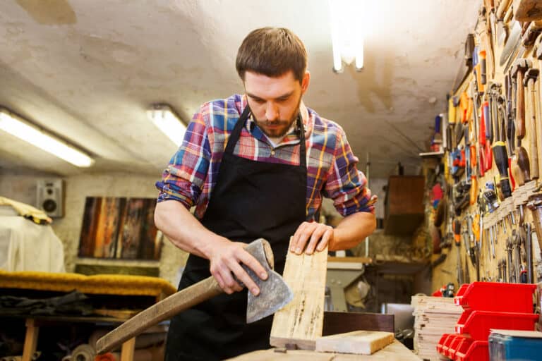 profession, carpentry, woodwork and people concept - carpenter with axe and wood plank working at workshop